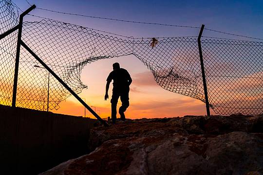 Un rifugiato cammina oltre la recinzione della frontiera Ue_Canva